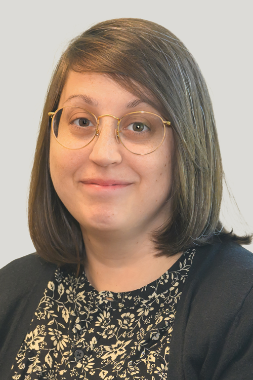 Woman with shoulder length straight brown hair and glasses looks at camera with a slight smile.